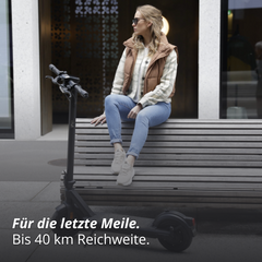 Frau sitzt auf einer ank, vor ihr steht ein VMAX E-Scooter
